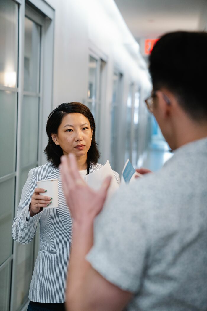 A woman looking intently at a man, holding a cup, possibly misreading social cues during a conversation.