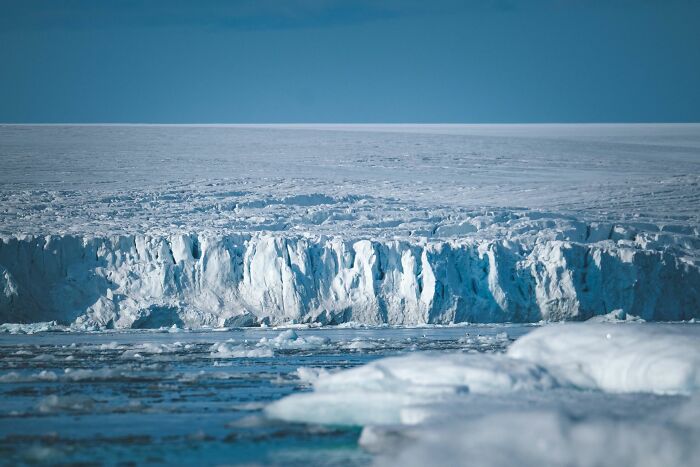 A vast ice sheet with a towering ice wall, reflecting the blue sky, representing unsolved mysteries in frozen landscapes.