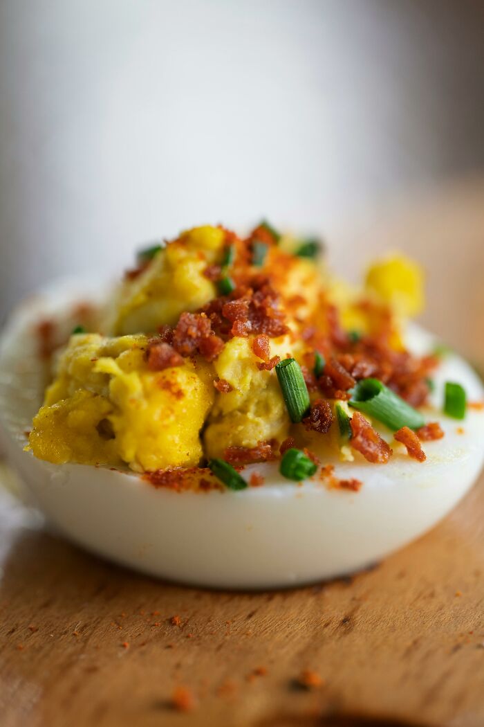 Close-up of deviled egg topped with bacon and chives