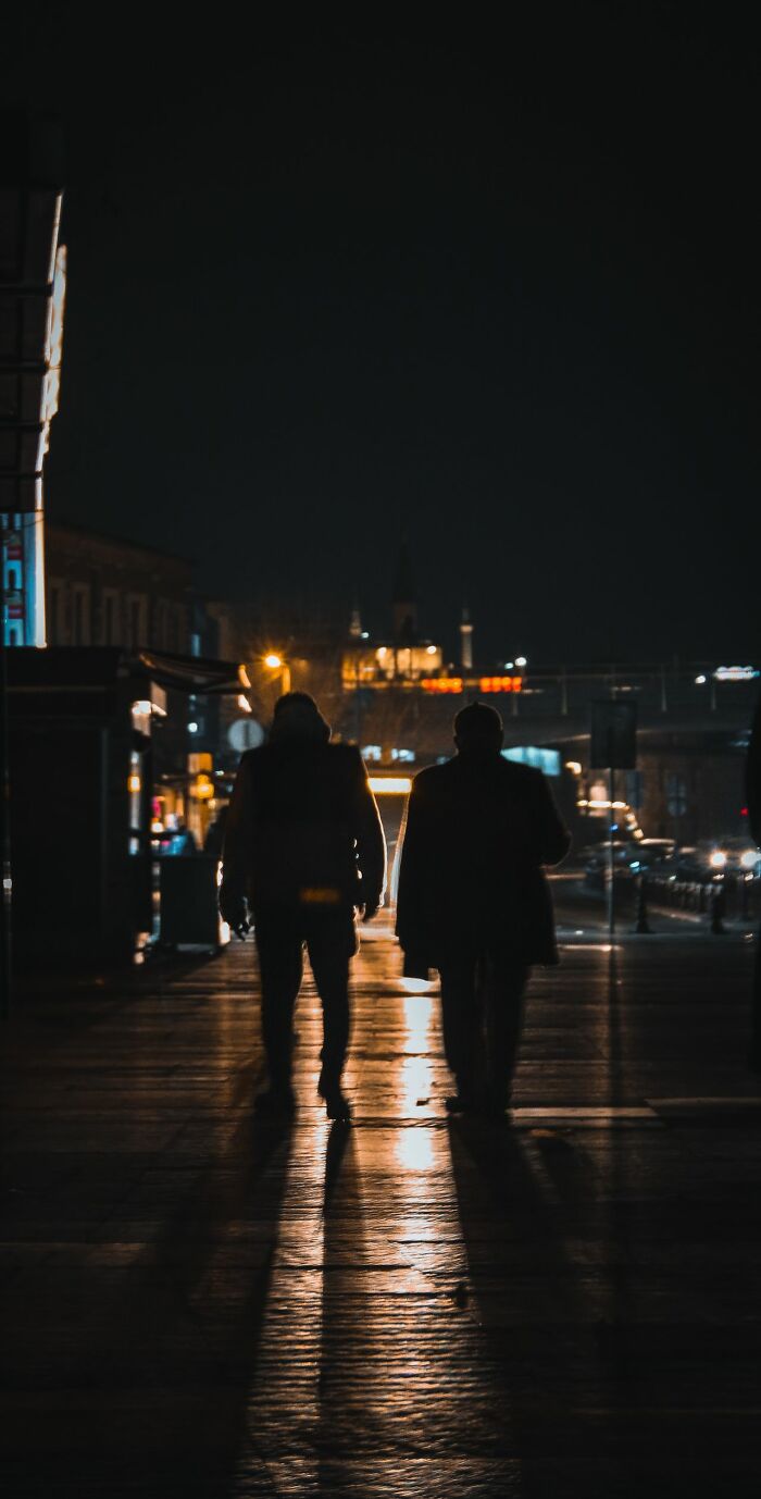 Two silhouettes walking on wet street at night with city lights