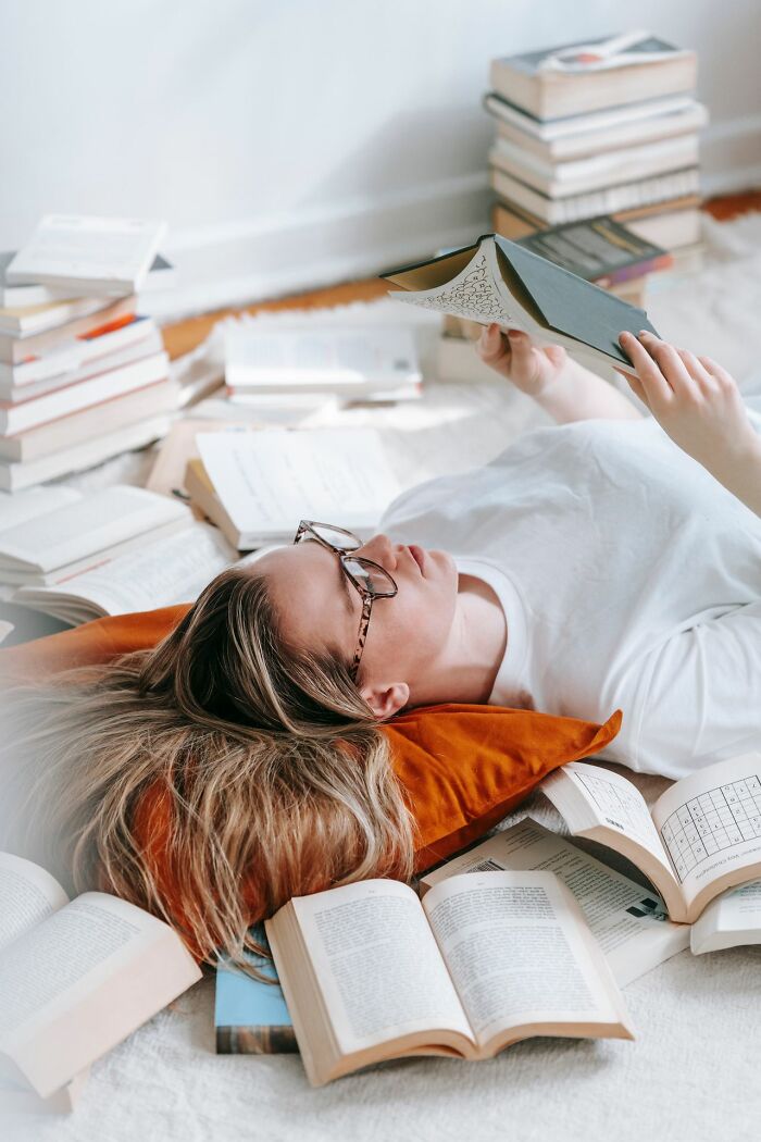 A person lying on the floor surrounded by books, showing hints of being secretly very smart.