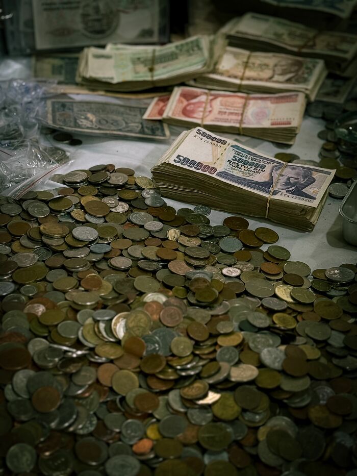 A large pile of coins and stacks of international banknotes, representing the financial aspects of hidden true selves.