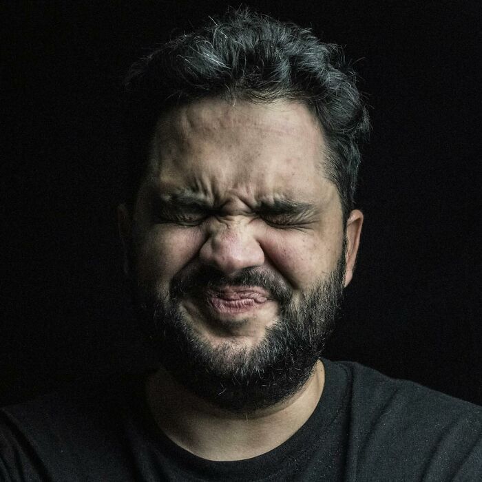 Man grimacing with eyes closed against black background