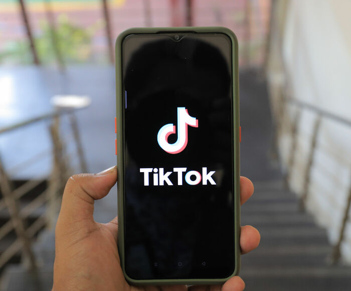 A hand holding a smartphone displaying the TikTok app logo, representing social media and dangerous challenges.