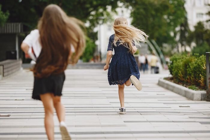 Girls running joyfully on city sidewalk with green trees