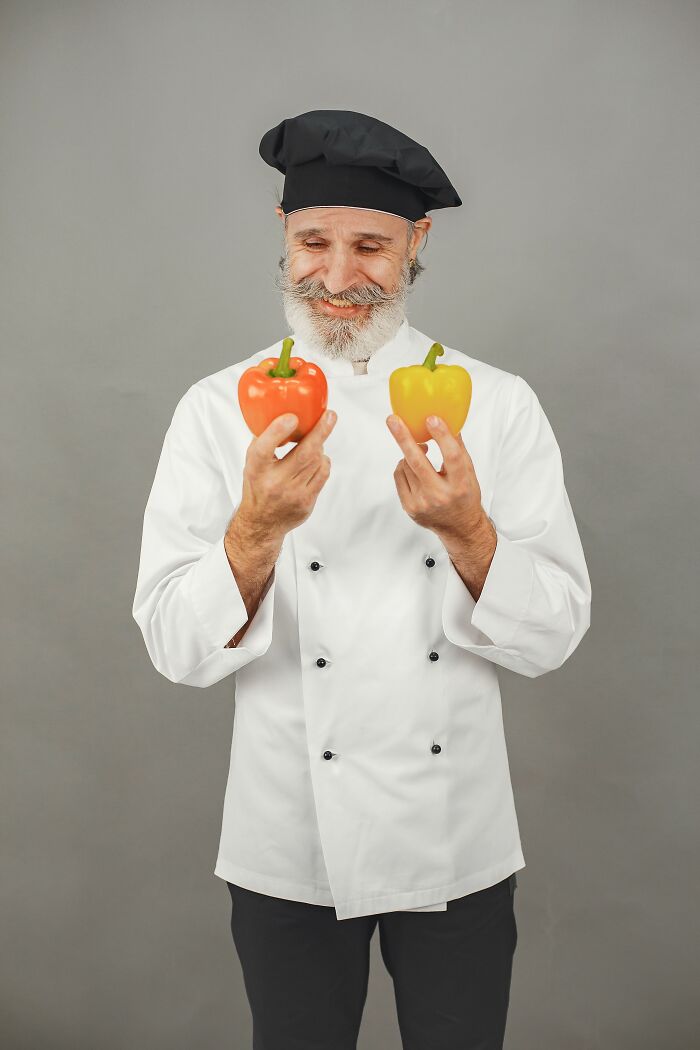 A smiling chef in a white uniform and black hat holding a red and yellow bell pepper, representing experiences people can't explain.