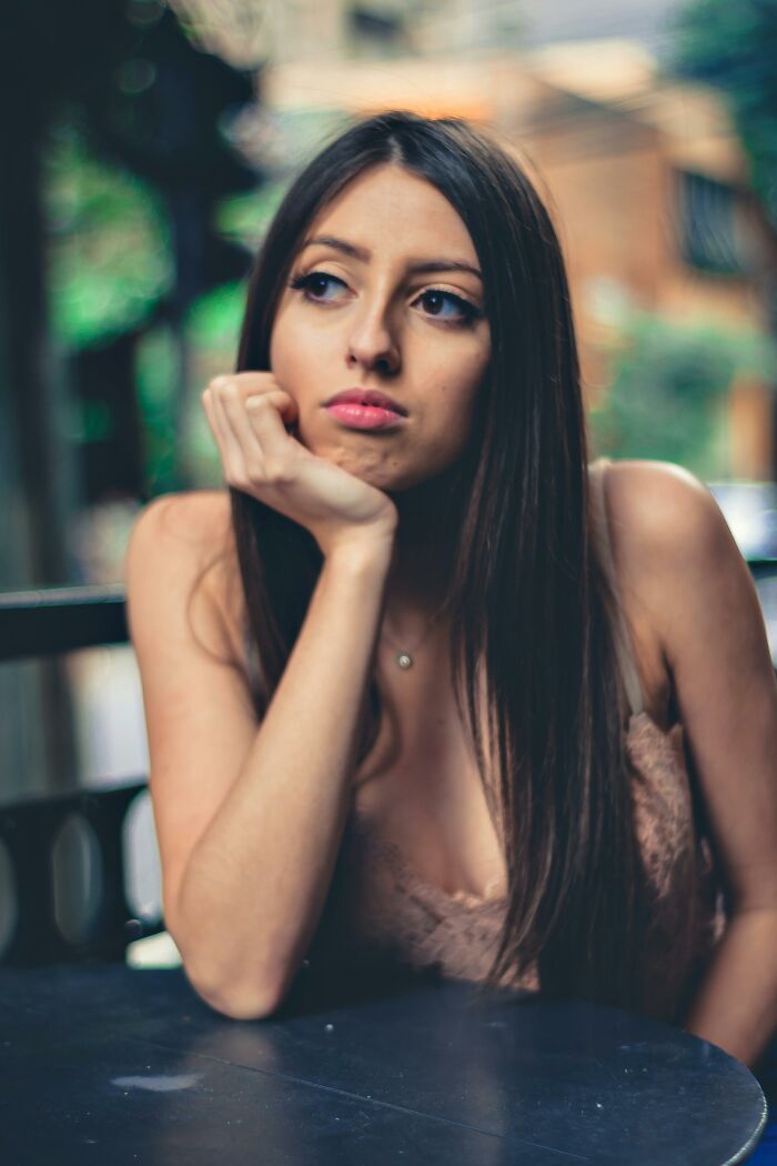 Pensive woman with long dark hair sitting at table outdoors