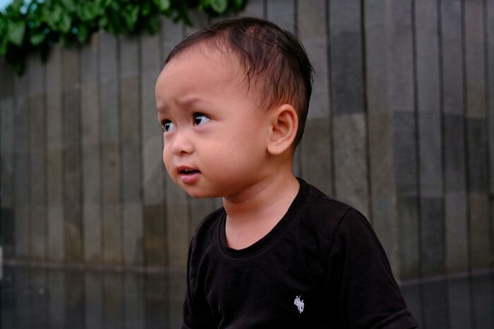 Curious toddler with confused expression wearing black shirt against stone wall background
