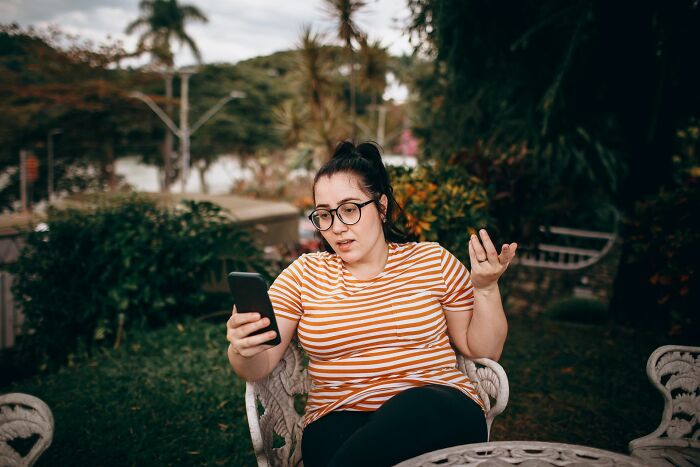 Woman looking frustrated at phone while sitting outside at garden table