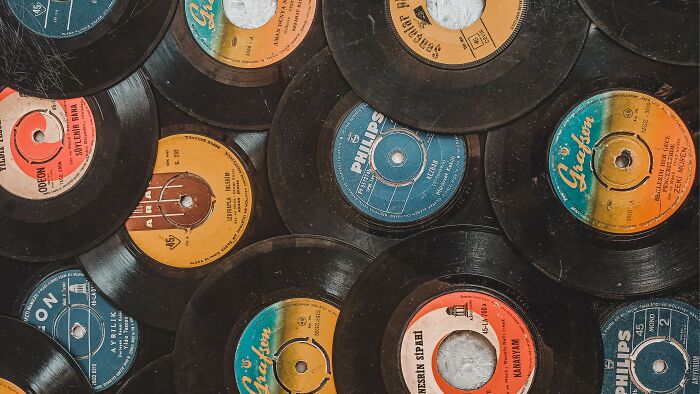 A close-up view of vintage 45 RPM vinyl records, stacked, featuring colorful labels and title mashups. A close-up view of vintage 45 RPM vinyl records, stacked, featuring colorful labels and title mashups.