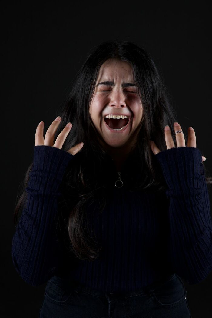 Person screaming with eyes closed and hands raised on black background
