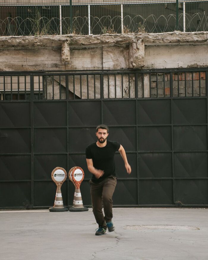 Man running on concrete surface in front of black metal gate with barbed wire above