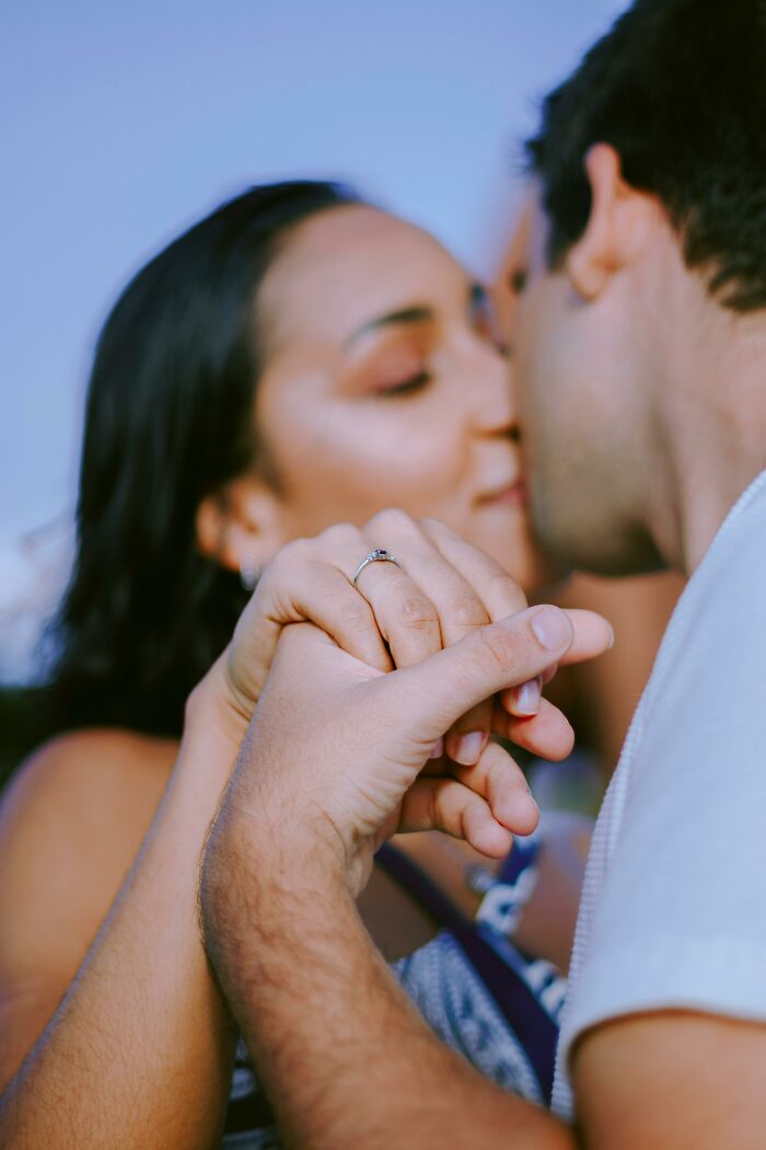 Couple holding hands showing engagement ring with kiss