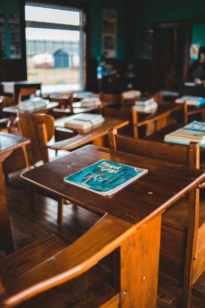 An old textbook rests on a wooden desk in an empty classroom, sun streaming through the window. People hid their true selves.
