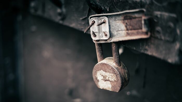 A rusted padlock on a dark, weathered surface, symbolizing an unsolved mystery or a hidden secret.