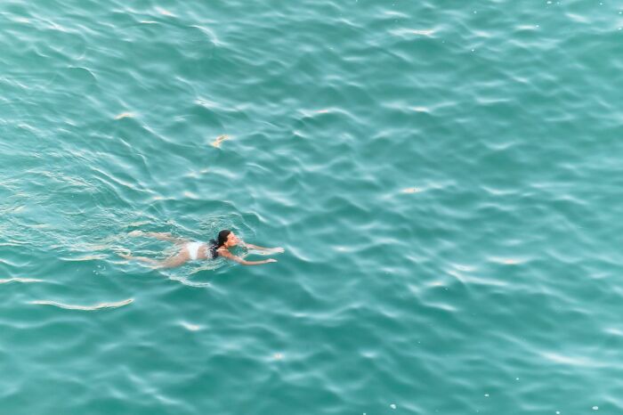 A person swimming alone in a vast expanse of blue ocean water, depicting something creepy.