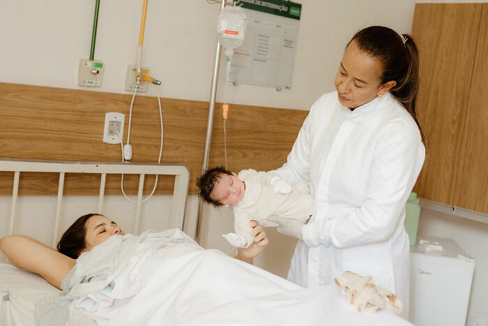 A nurse holding a newborn baby next to the mother in a hospital, a moment of profound coincidences.