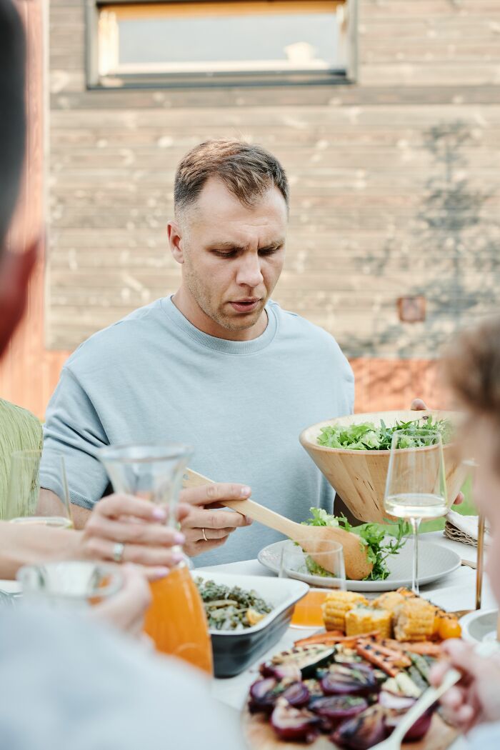 Man serving salad at outdoor meal with grilled vegetables