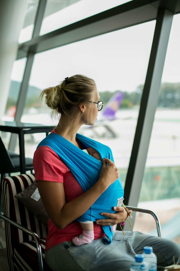 Mother with baby in carrier sitting by airport window before boarding