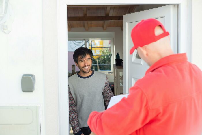 British delivery man handing parcel to smiling man at the front door