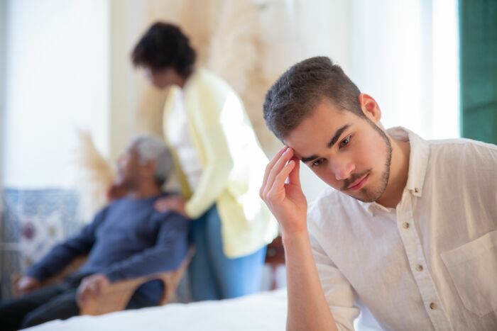 Young man looking stressed while family interacts in background showing moments men faced change