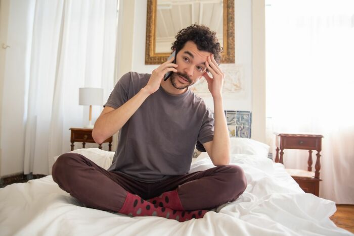 Man sitting on bed talking worried on phone at home