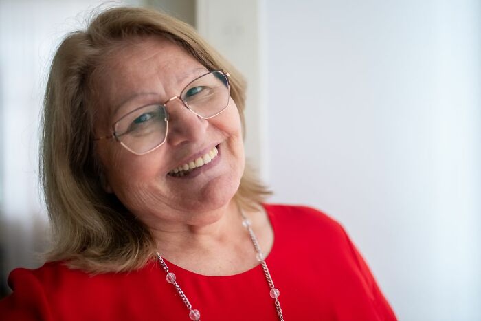 A happy, smiling older woman wearing glasses and a red top, listening to stories from polygamist families.