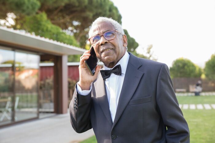 An older man in a suit talking on the phone, possibly a figure from a polygamist family's stories.