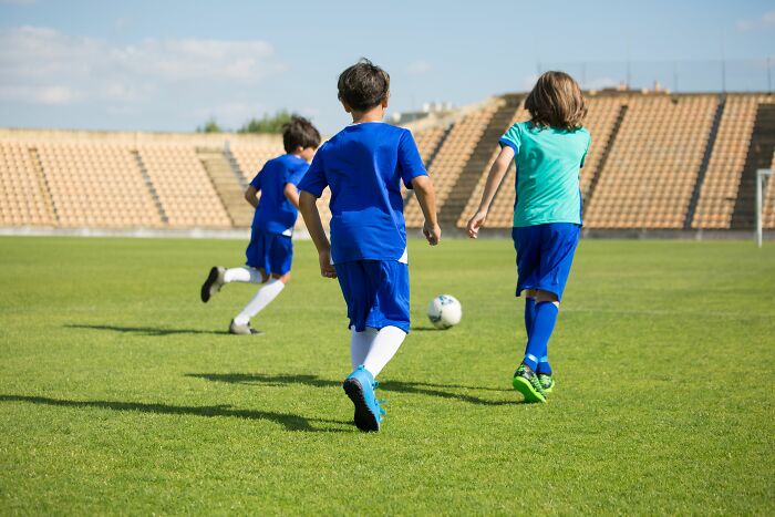 Three young boys in soccer uniforms running on a field with a ball, avoiding full rage mode during play.