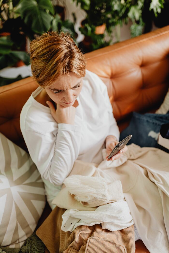 A woman looking at her phone with a confused expression, surrounded by clothes, experiencing wild coincidences.