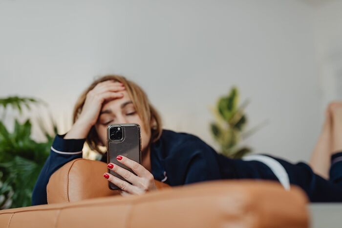 Stressed woman lying down looking at phone after infidelity discovery
