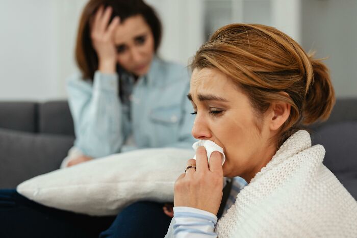 Sad woman crying with a tissue while another woman comforts her