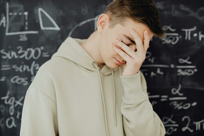 Student covering face stressed in front of chalkboard with scientific formulas