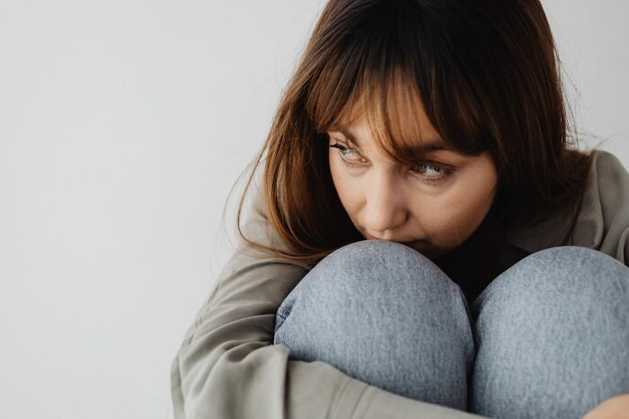 A woman looking distressed, hugging her knees, experiencing something creepy.
