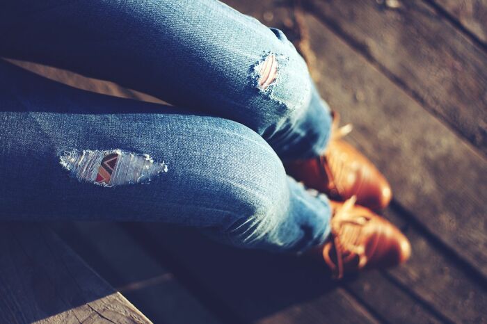 Closeup of ripped jeans and brown shoes on wooden surface