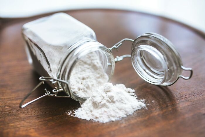 Glass jar spilled with white baking powder on wooden surface