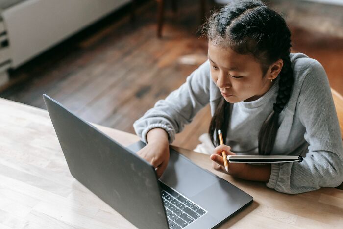 Young girl studying general knowledge questions on laptop with notebook and pencil