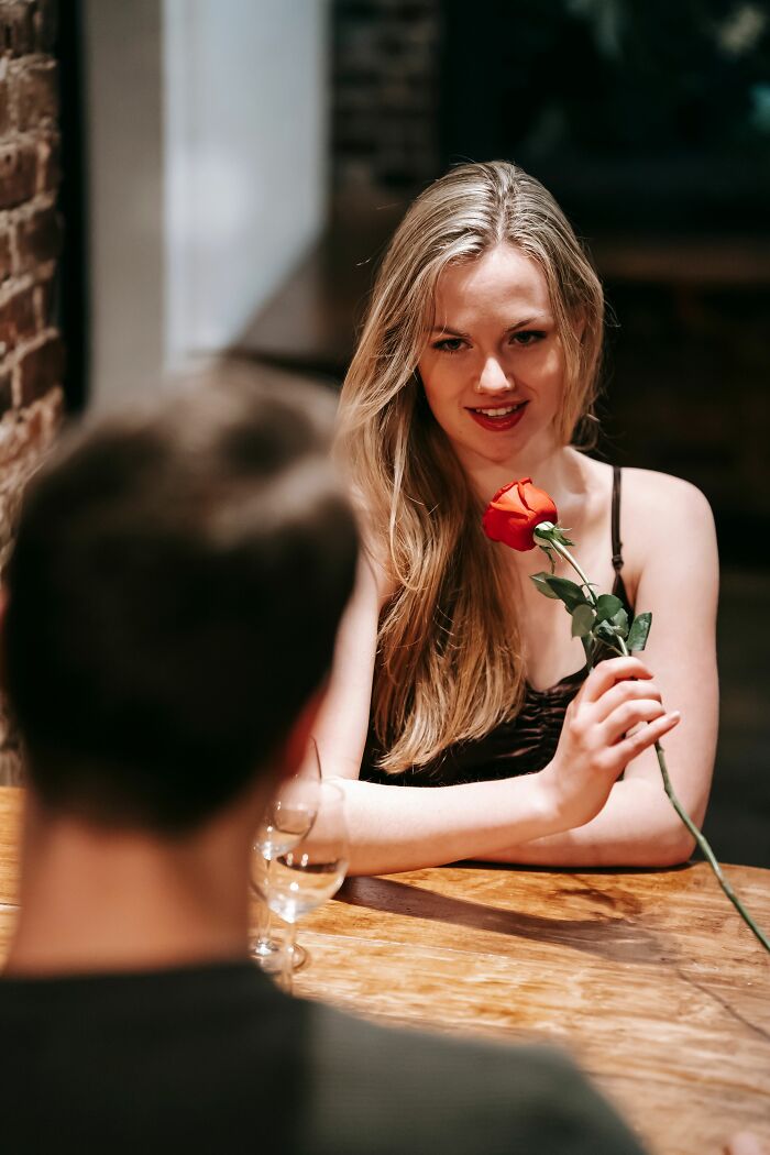 A woman smiling, holding a red rose, showing men's turn offs women roll their eyes at.