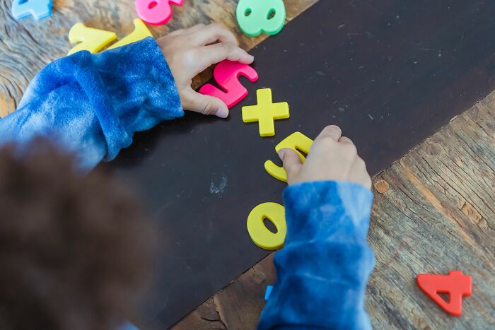 Child arranging colorful numbers and math symbols for math puzzles on wooden table Child arranging colorful numbers and math symbols for math puzzles on wooden table