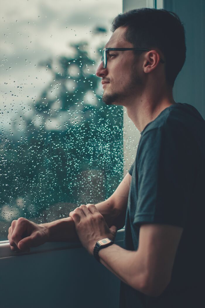Man with glasses looking out window on rainy day