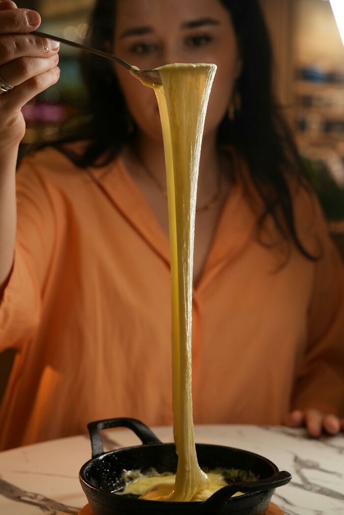 Woman lifting stretchy melted cheese from skillet