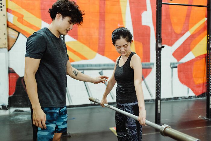 Man helping a woman with a barbell at the gym, discussing turn offs.