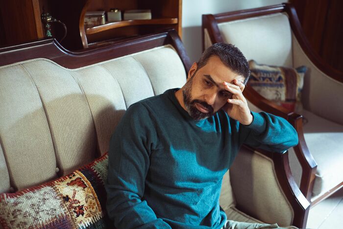 Man sitting on couch looking stressed and thoughtful at home