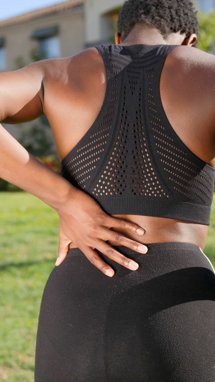 A person with a sports bra holds their lower back, experiencing types of pain they won't comprehend.