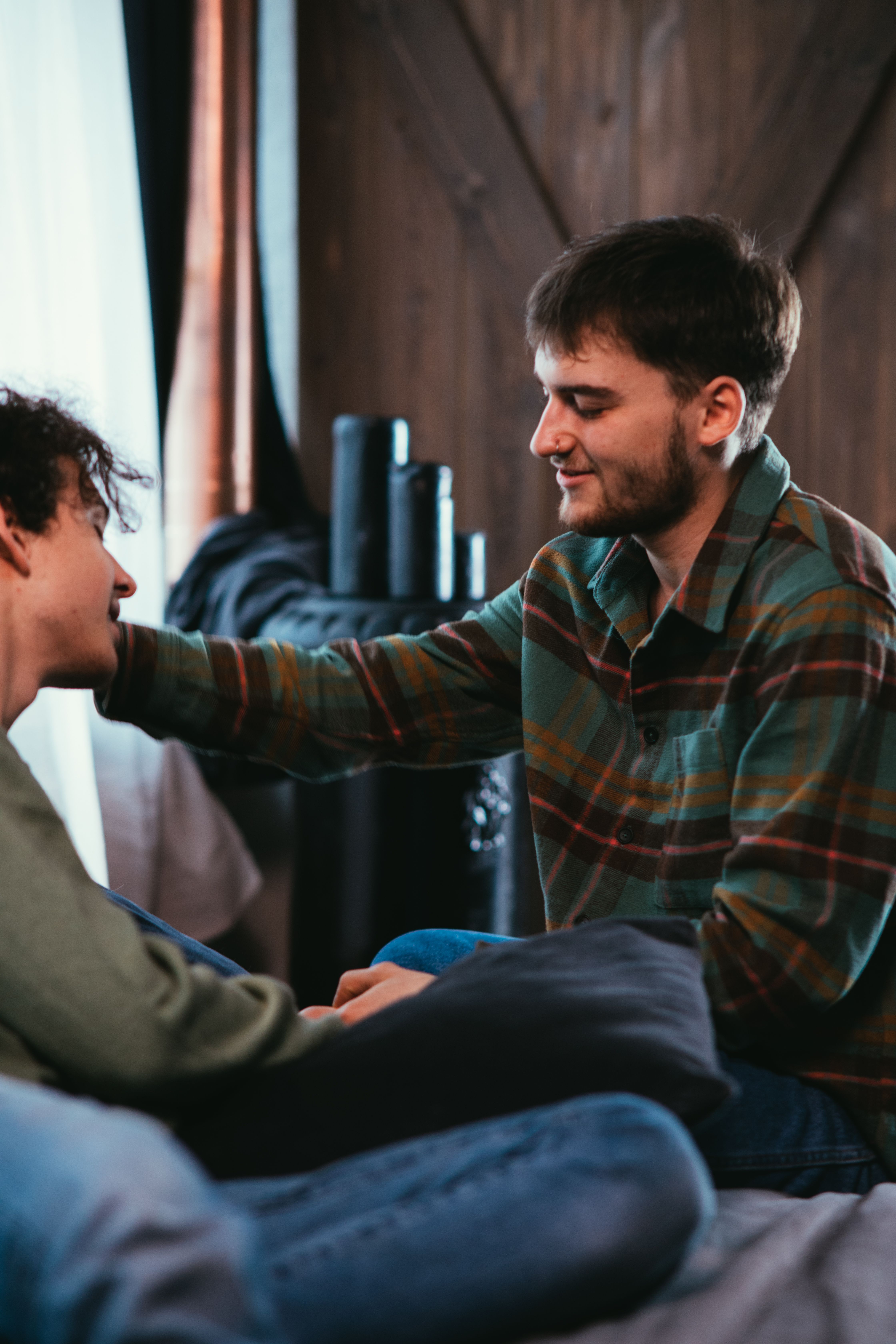 A man with a beard in a plaid shirt gently touches the face of another man, revealing a husband's double life.