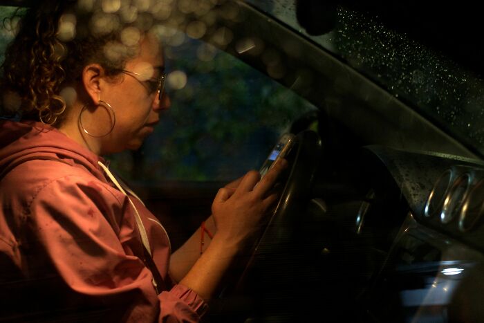 Woman texting on phone in car at night possibly about cheating