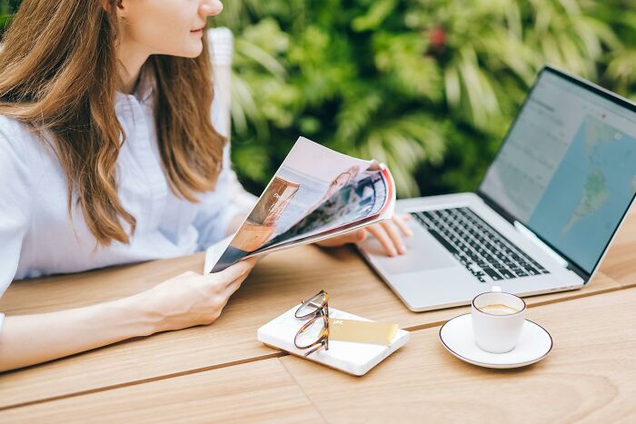 Woman reading magazine with laptop and coffee cup outdoors