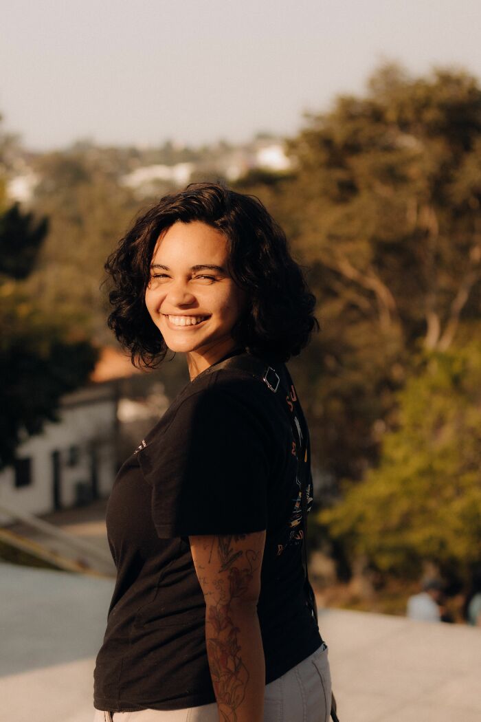 A happy woman with short dark hair smiling over her shoulder outdoors, showing men's turn offs women roll their eyes at.