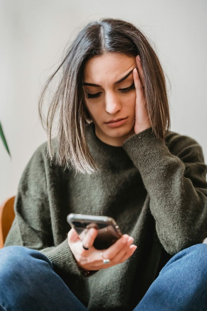 A young woman looking distressed while holding her phone, illustrating stories from polygamist families.