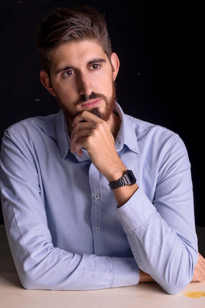 A thoughtful man, showing hints of being very smart, with a beard and light blue shirt, hand on chin.